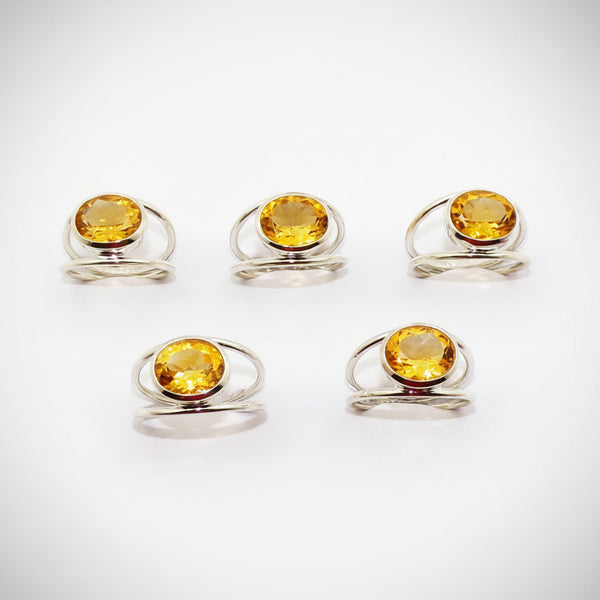 Silver rings with yellow gemstones on a white surface with floral decorations.